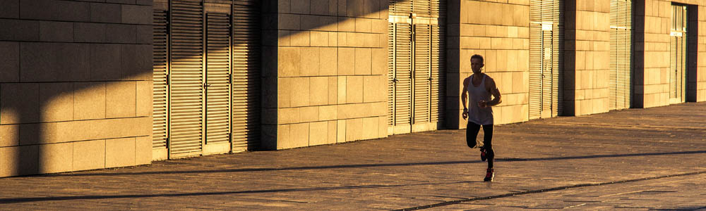Fit man running down an alley between two buildings, sunlight is streaming in so the background is splashed in yellow light